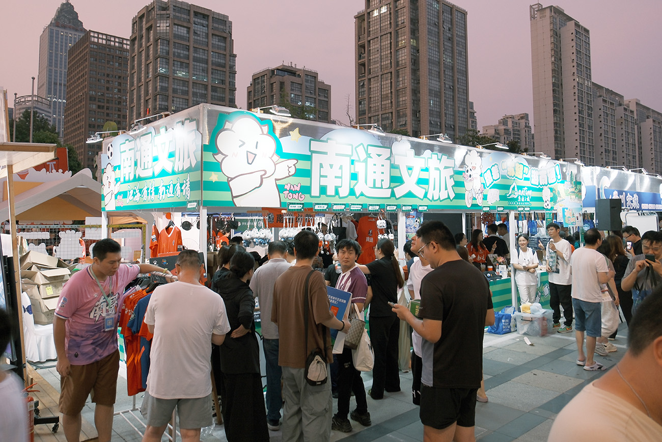 圖2：南通文旅攤位，「通通」蘇超玩偶、狼狼玩偶，藍(lán)印花布蘇小狼等南通好物吸引球迷觀眾排隊(duì)購買。.jpg